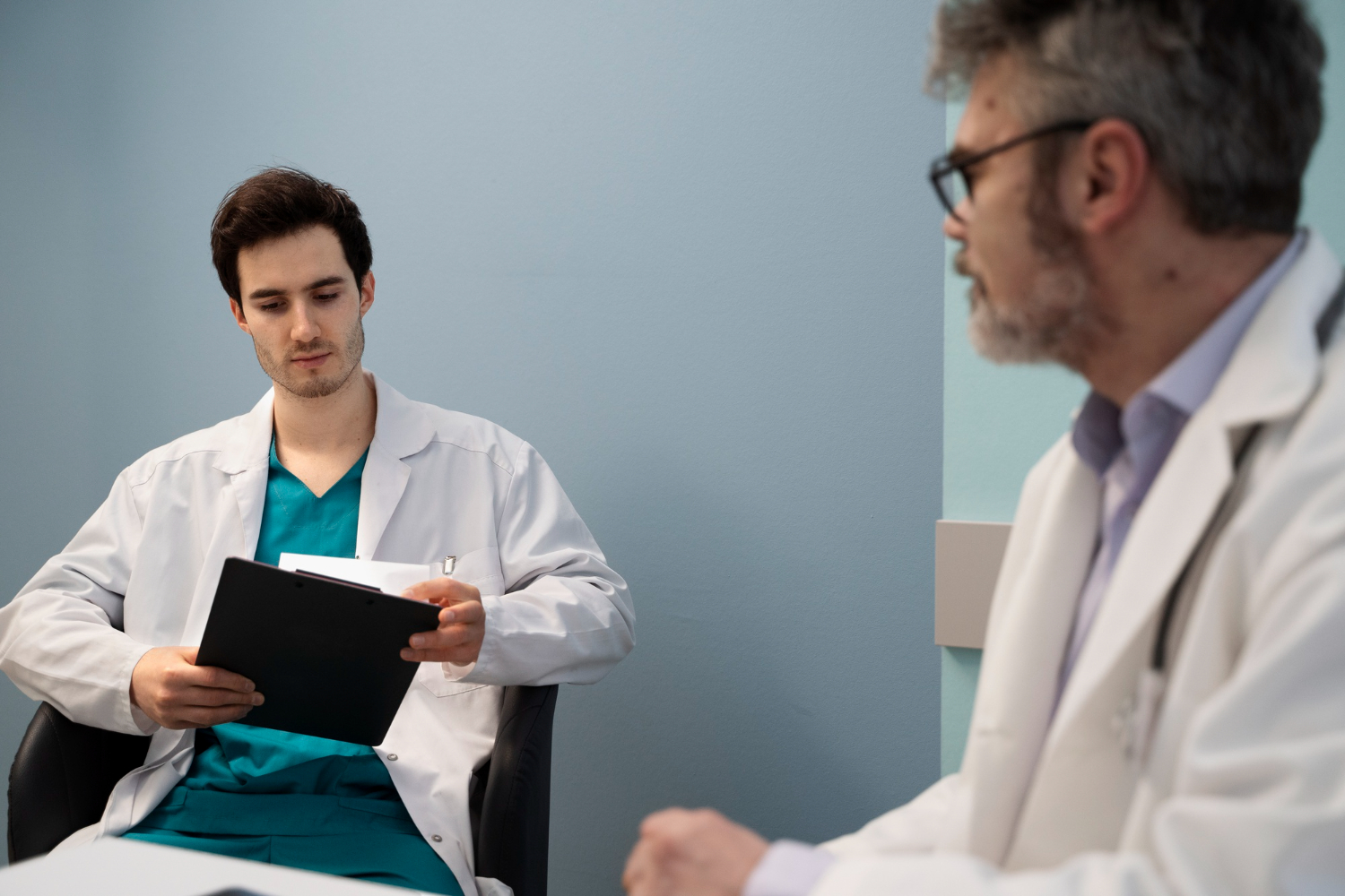 Dois médicos sentados discutindo sobre políticas e procedimentos no atendimento ao paciente.